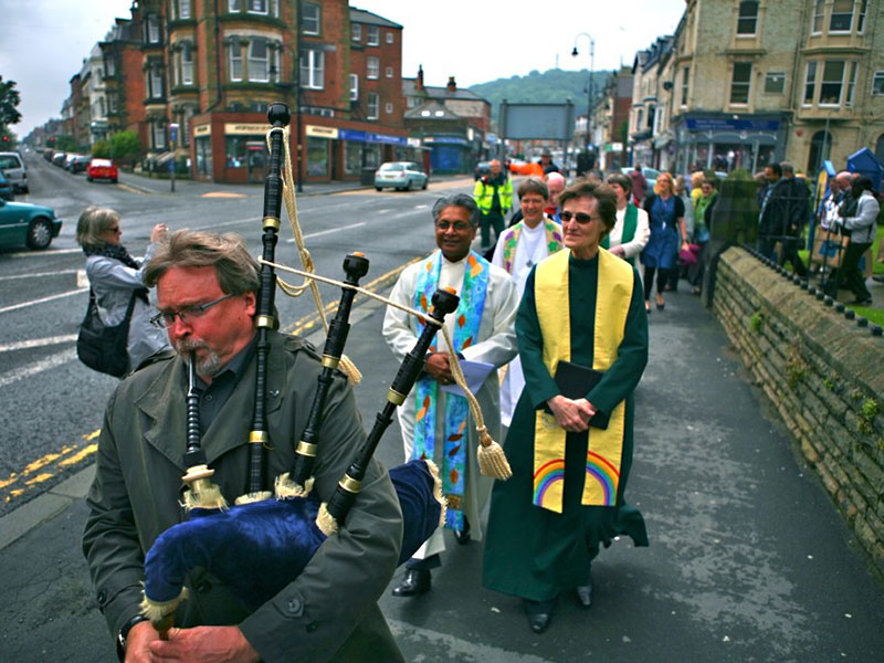 Bagpiper leading a procession of people along a road