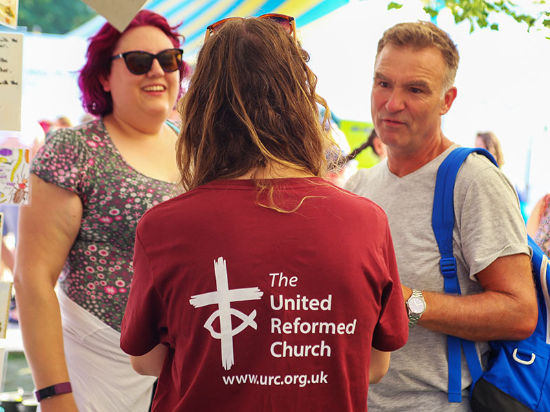 Three people, one wearing a URC t-shirt, standing and chatting